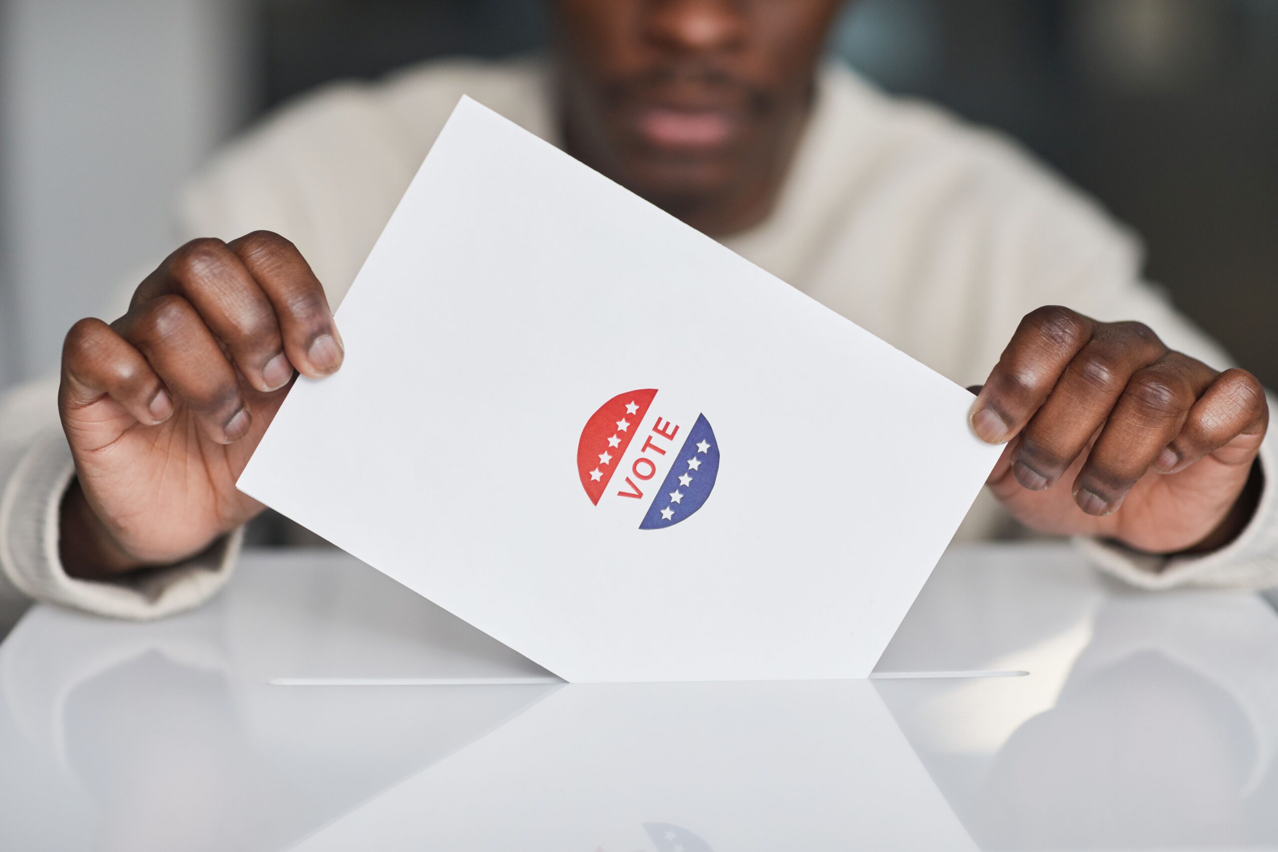 Photo of ballot held by two hands with person out of focus in the background // pexels-edmond-dantes